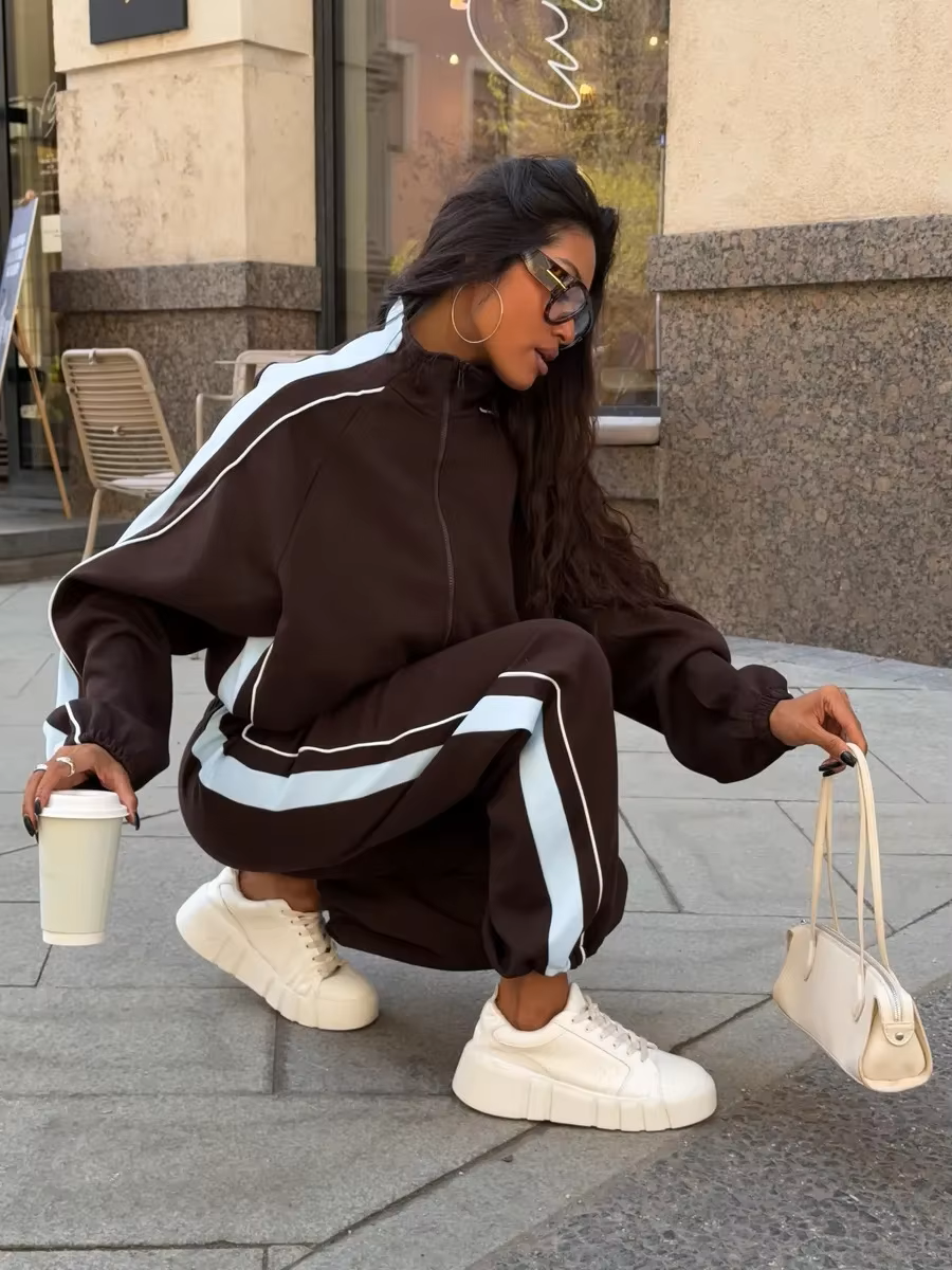 Chocolate brown track jacket and wide-leg pants set with light blue side stripes styled with a white handbag