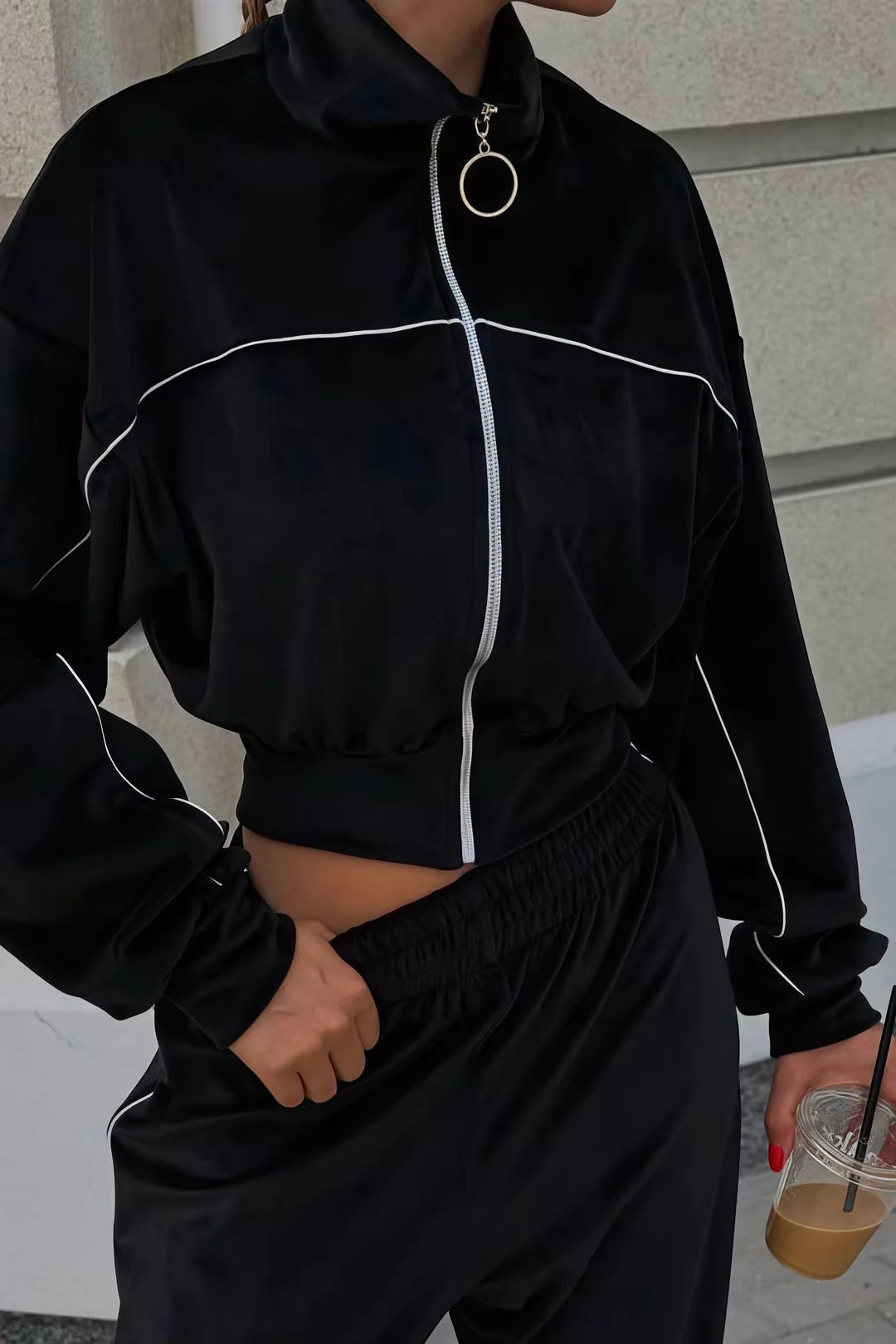 Black contrast-piping tracksuit close-up showing high collar, ring zipper and elasticated waistband